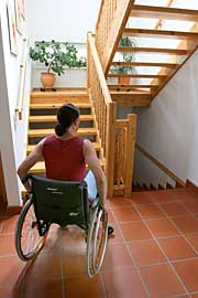 Themenfoto: Eine Frau im Rolli steht vor eine unüberwindbaren Treppe