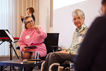 Talkrunde Highlights - Moderation durch Ninia LaGrande.  Sie sitzt auf der Bühne neben Prof. Dr. Sigrid Arnade. Im Hintergrund die Gebärdensprachdolmetscherin