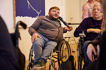 Blick ins Publikum - Redebeitrag von Alexander Ahrens, Interessenvertretung Selbstbestimmt Leben in Deutschland ISL e. V. Er sitzt dabei lässig im Rollstuhl.